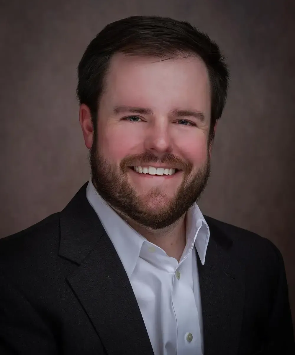 A man with a beard is wearing a suit and smiling for the camera.