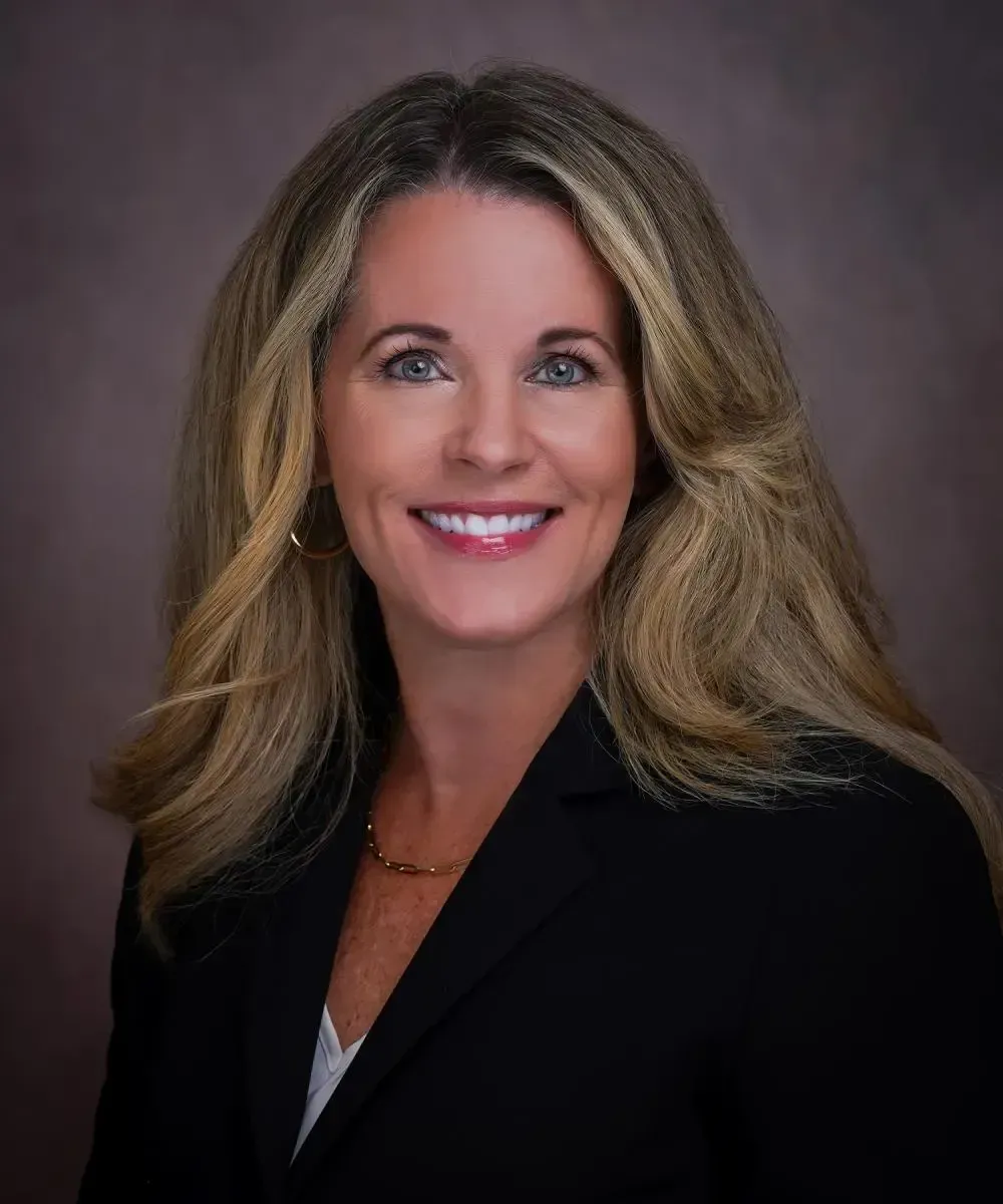 A woman in a black jacket and white shirt is smiling for the camera.
