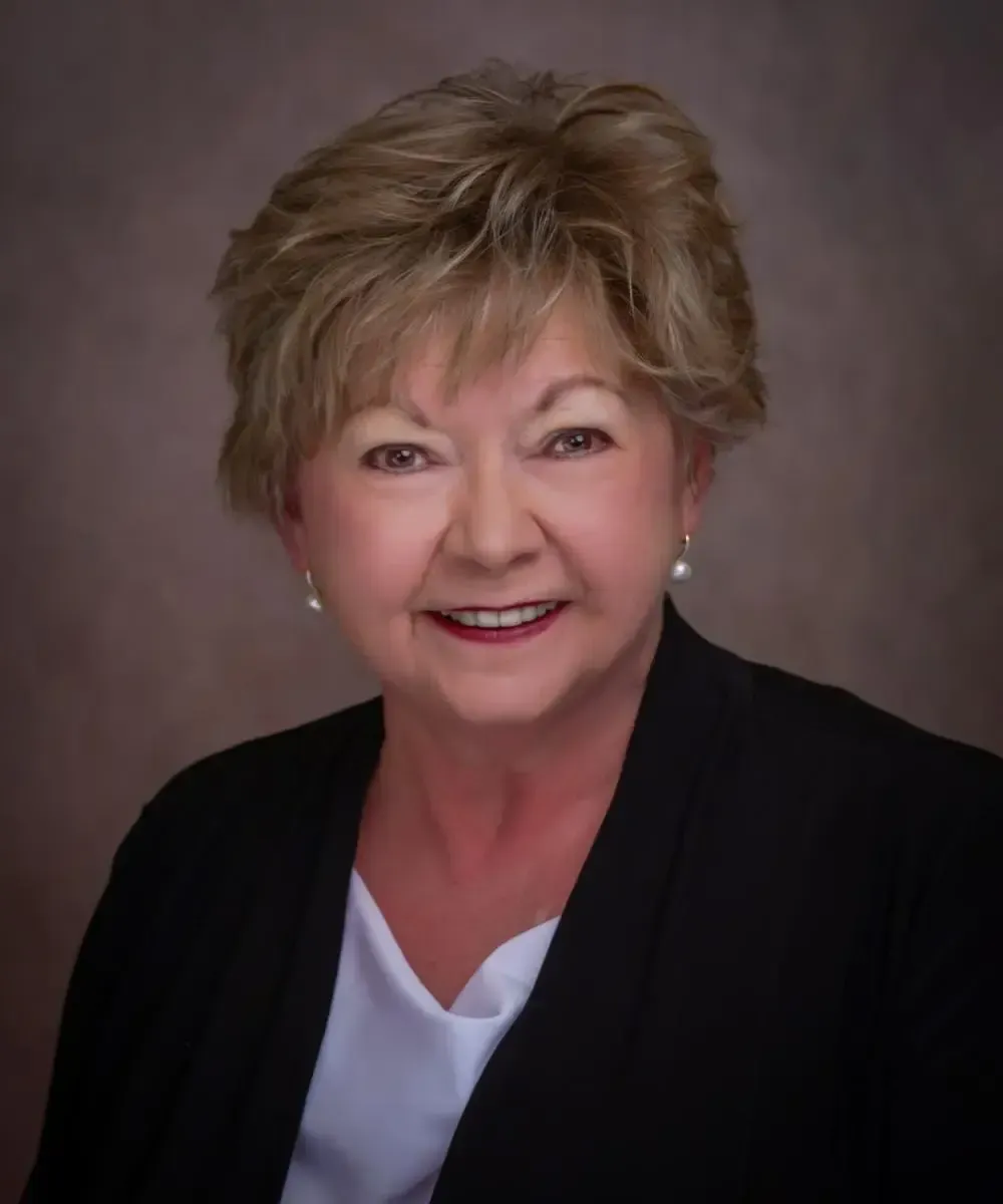 A woman in a black jacket and white shirt is smiling for the camera.