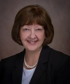 Julie Mitchell in a blue shirt and necklace is smiling in a circle.
