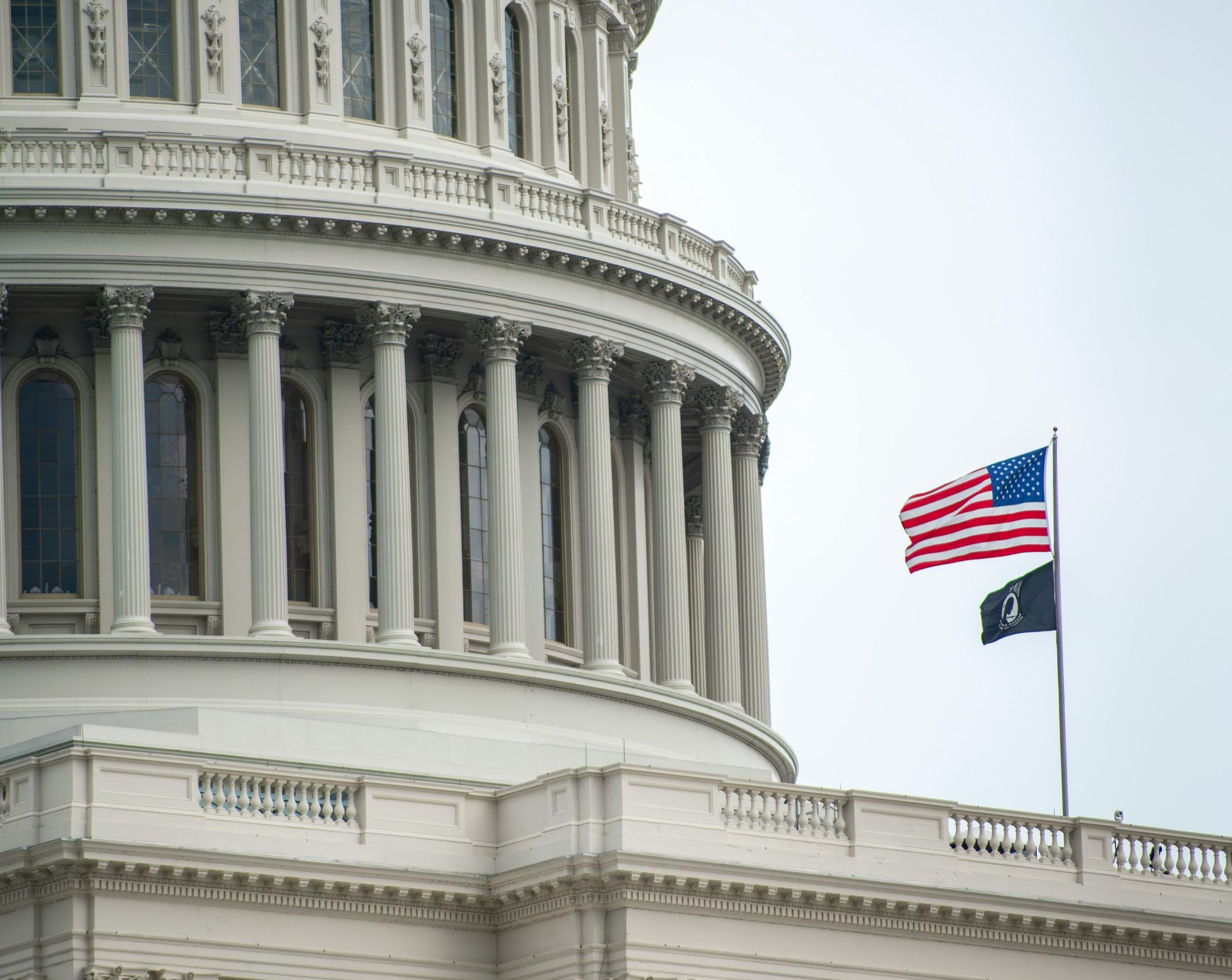 The U.S. Capitol dome with the American flag flying on a pole against a cloudy sky.