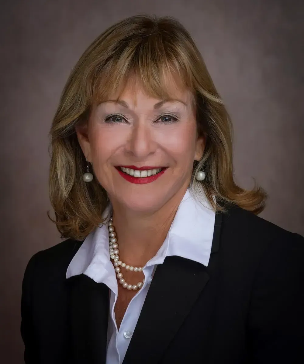 A woman in a suit and pearls is smiling for the camera.