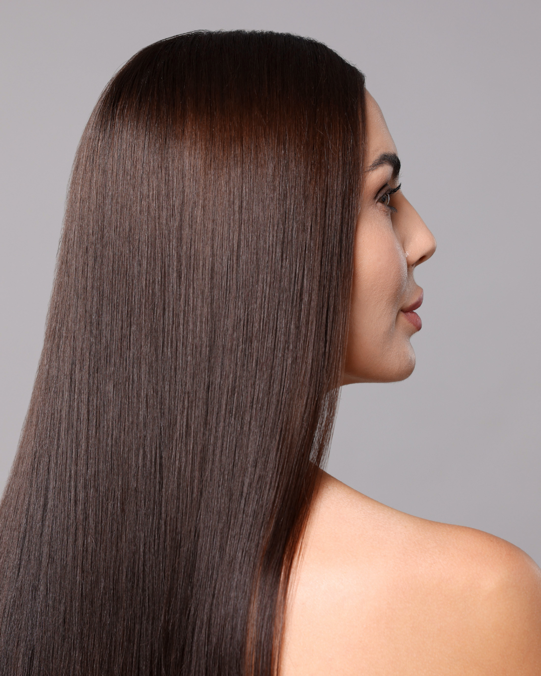 Femme aux longs cheveux bruns foncés, raides, tournée sur le côté et regardant vers la droite. Fond gris.