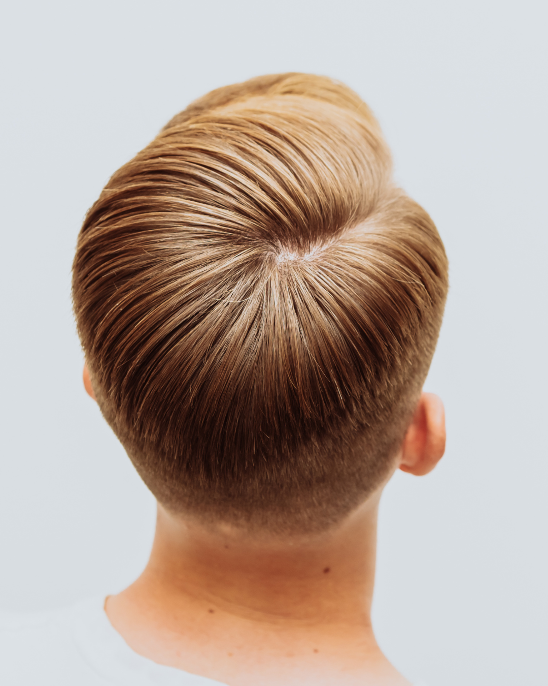 Gros plan sur la tête d'une personne, montrant une coiffure avec des côtés courts et dégradés et un dessus texturé coiffé en arrière.