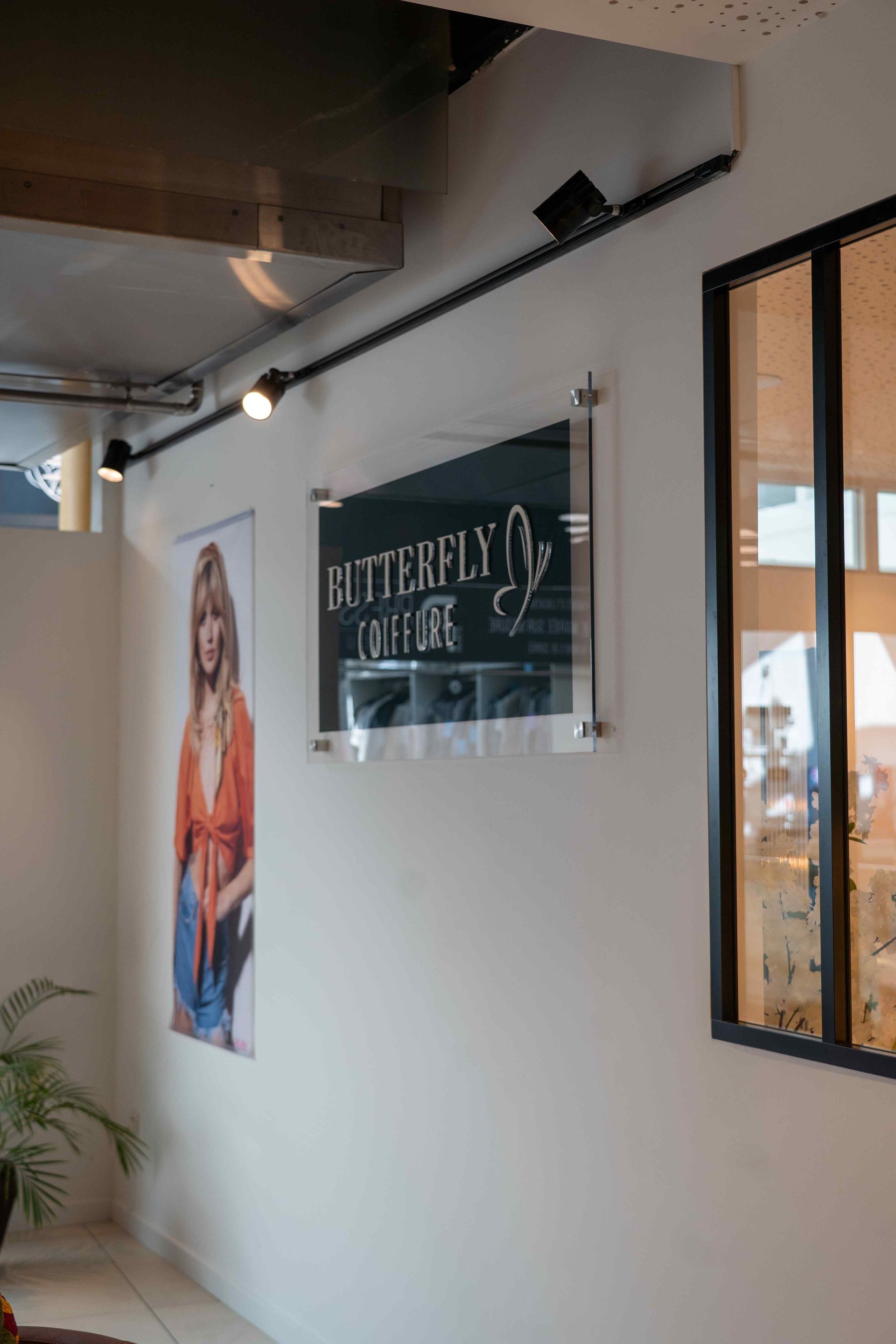 Enseigne pour Butterfly Coffee avec projecteurs, affiche d'une femme et fenêtre sur un mur blanc.