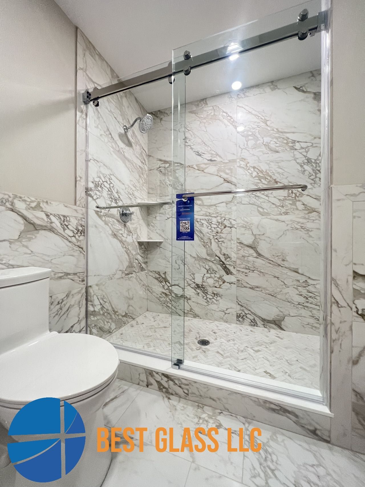 A bathroom with marble walls , a toilet , and a sliding glass shower door.