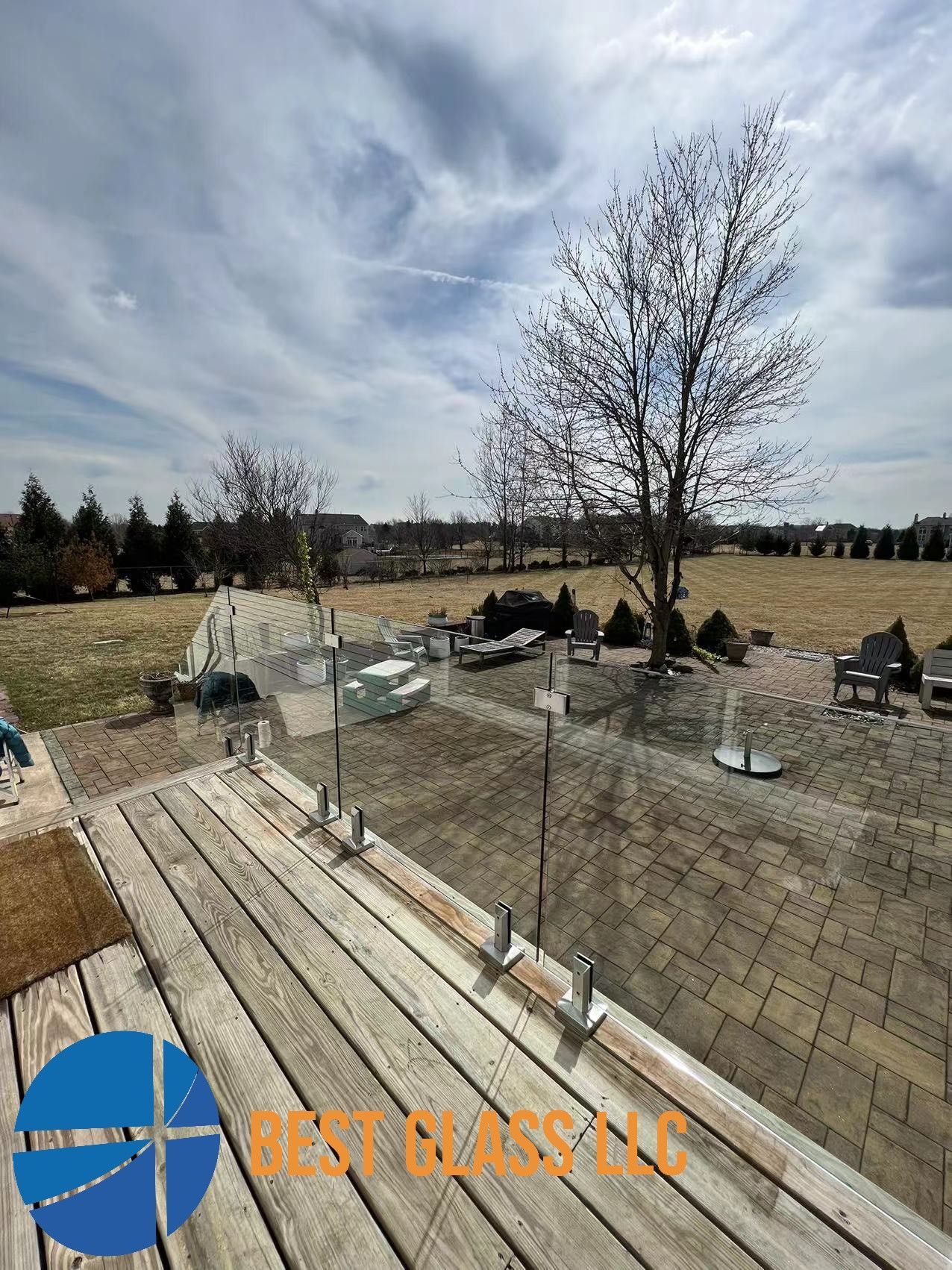 A wooden deck with a glass railing and a tree in the background.