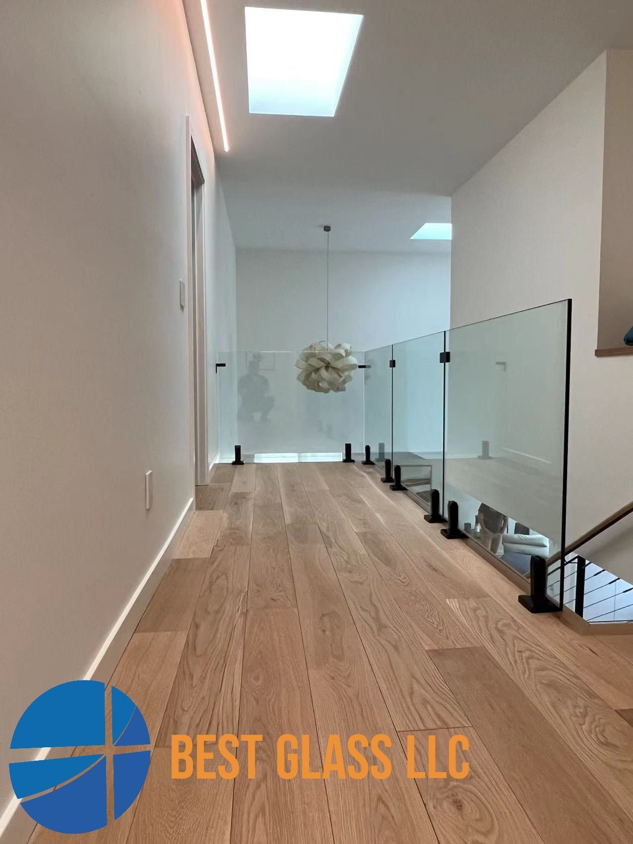 A hallway with hardwood floors and a glass railing from best glass llc