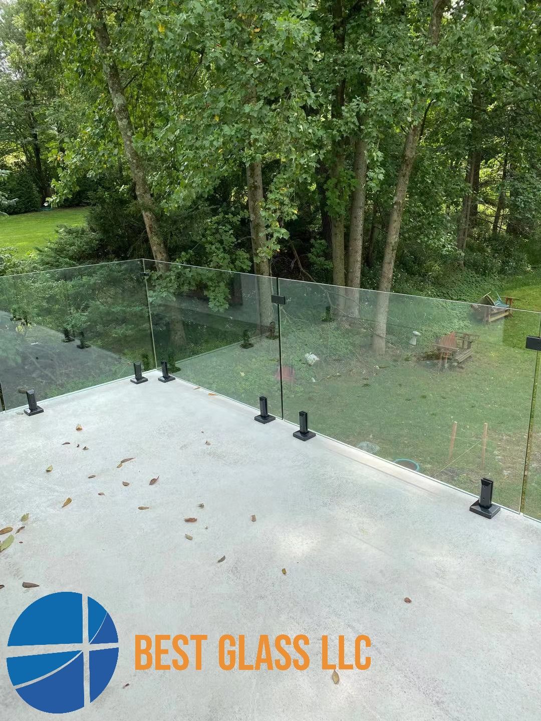A patio with a glass railing and a logo for best glass llc