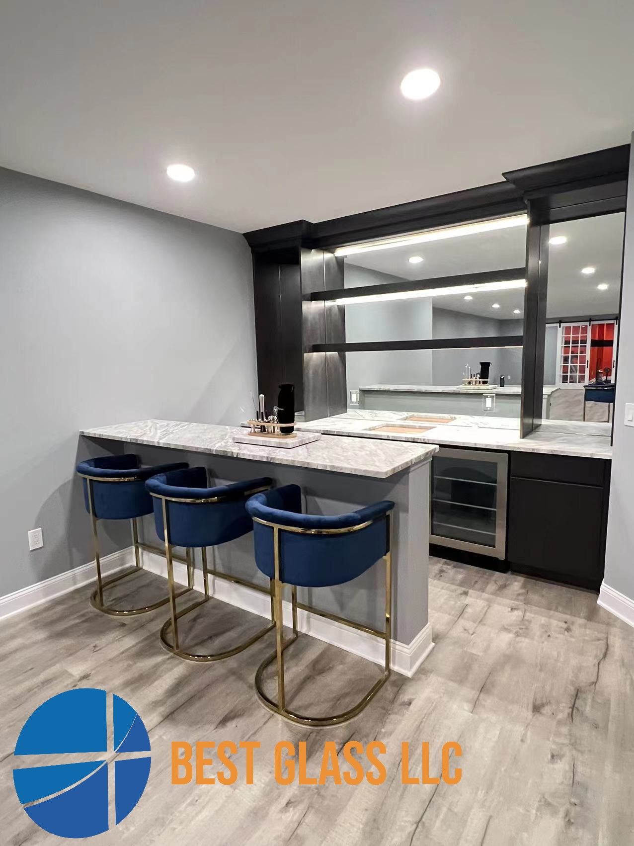 A basement with a bar , stools , a refrigerator and a large mirror.