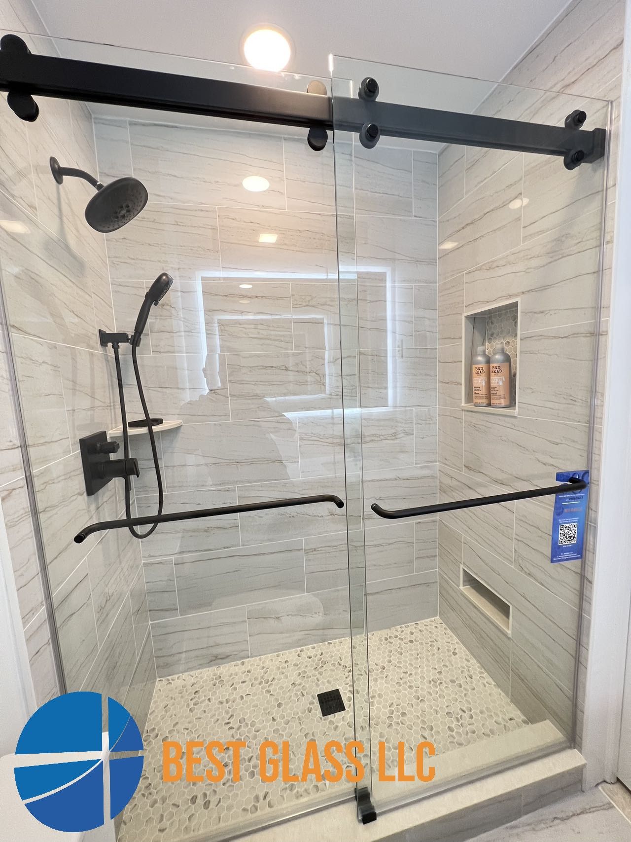 A shower with a sliding glass door and black handles.