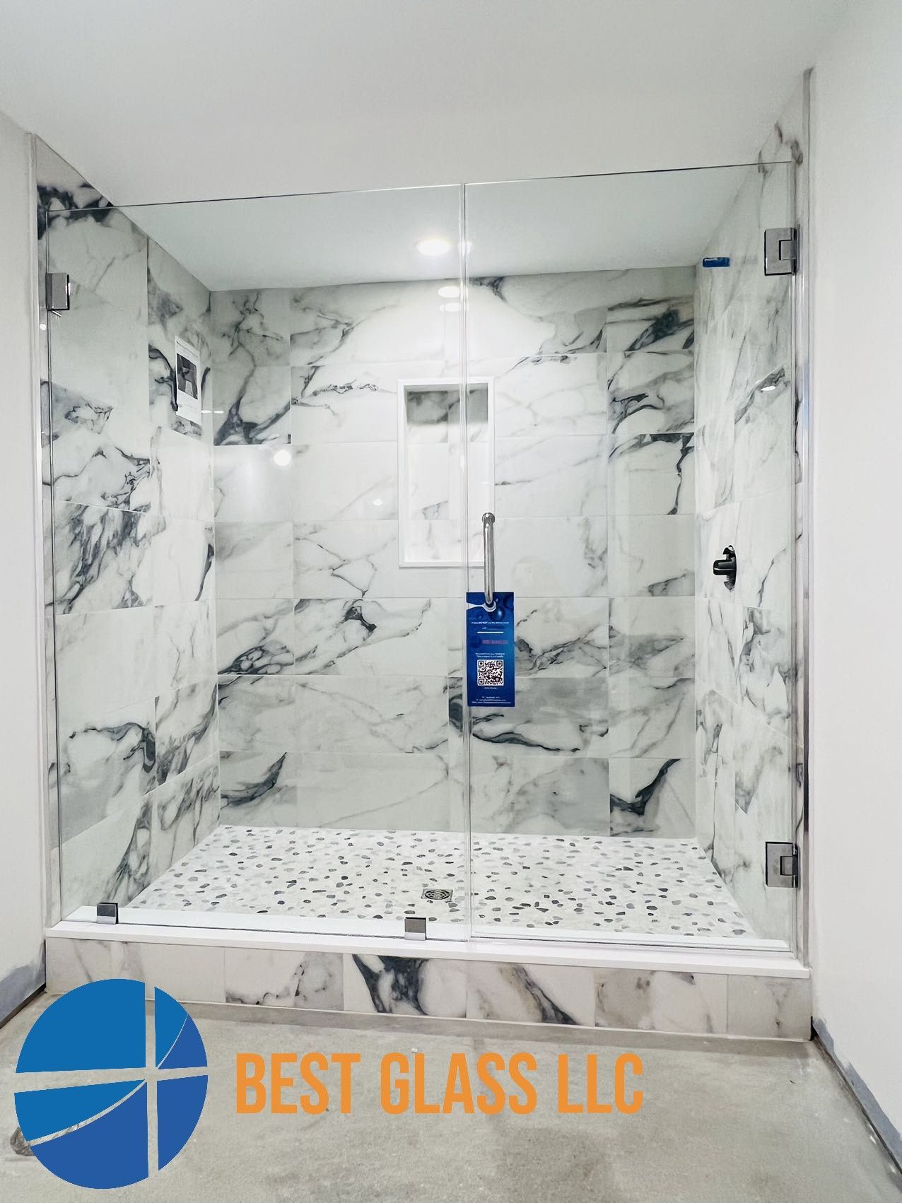 A shower stall with marble walls and a sign that says best glass llc