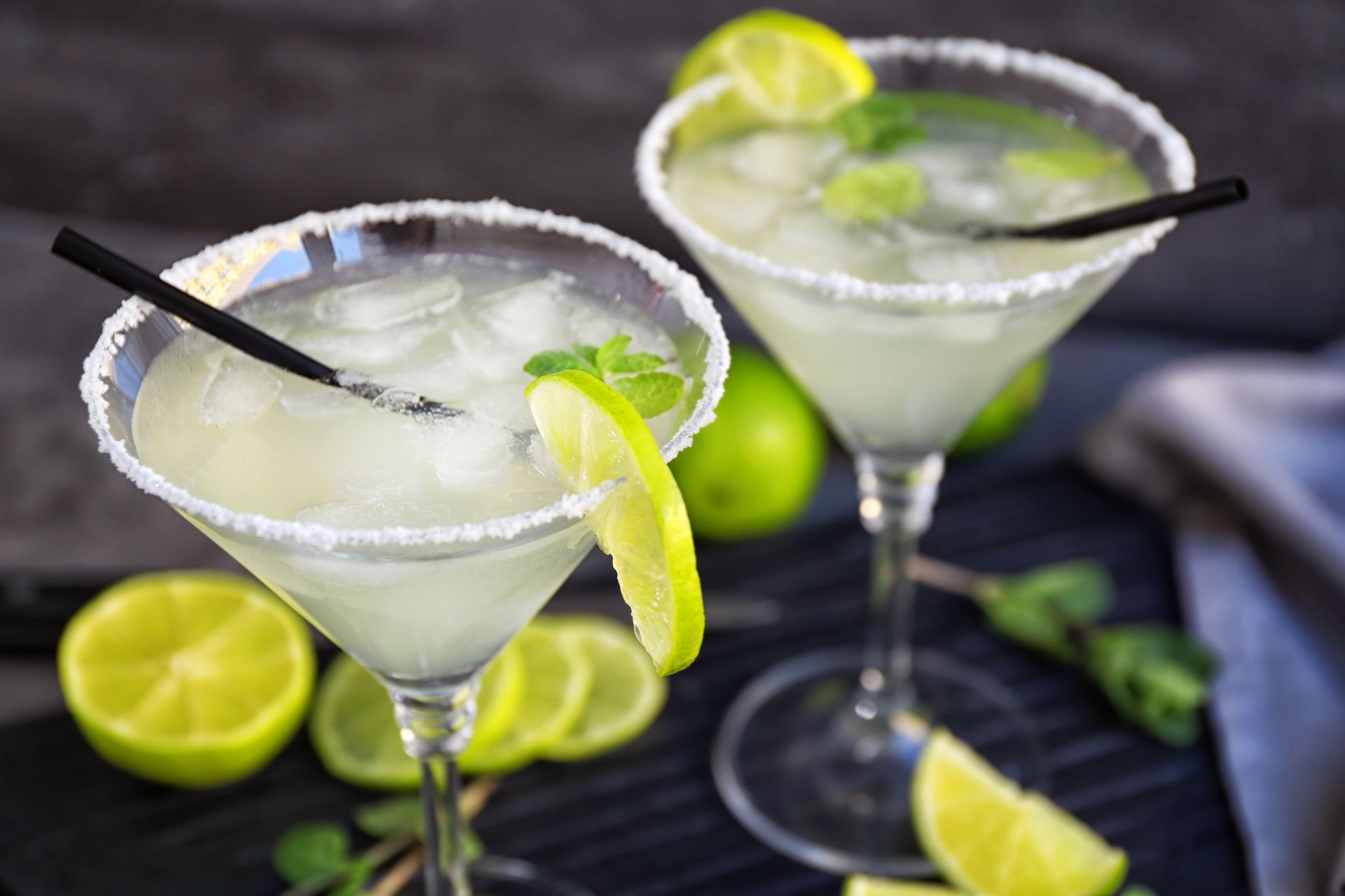 Two martini glasses filled with ice and lime slices on a table.