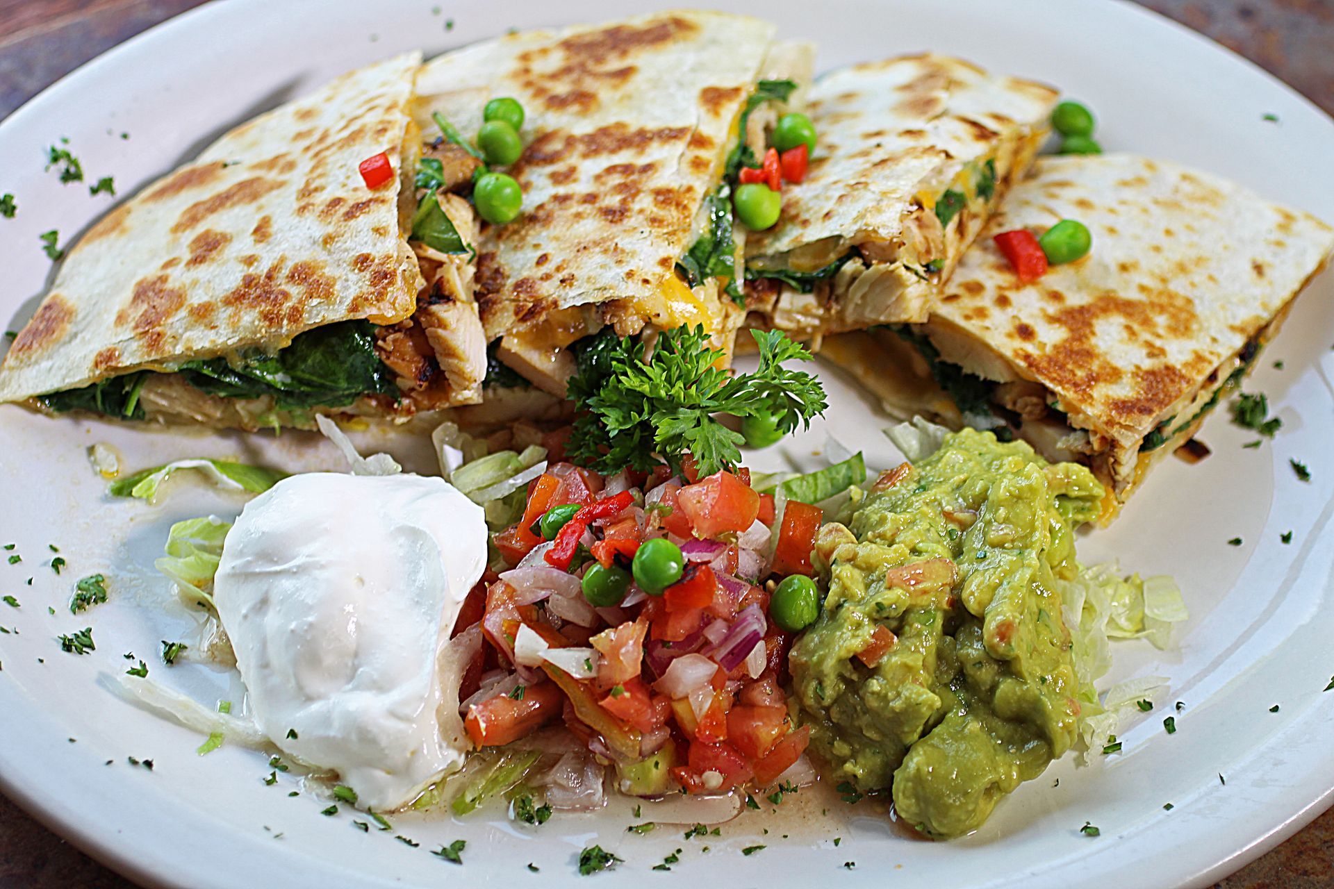 A white plate topped with quesadillas , guacamole , salsa and sour cream.