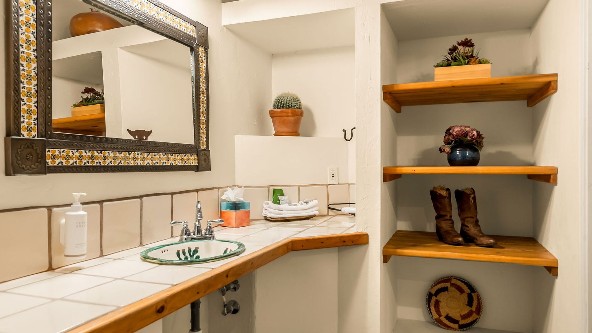 A bathroom with a sink , mirror , shelves and cowboy boots.