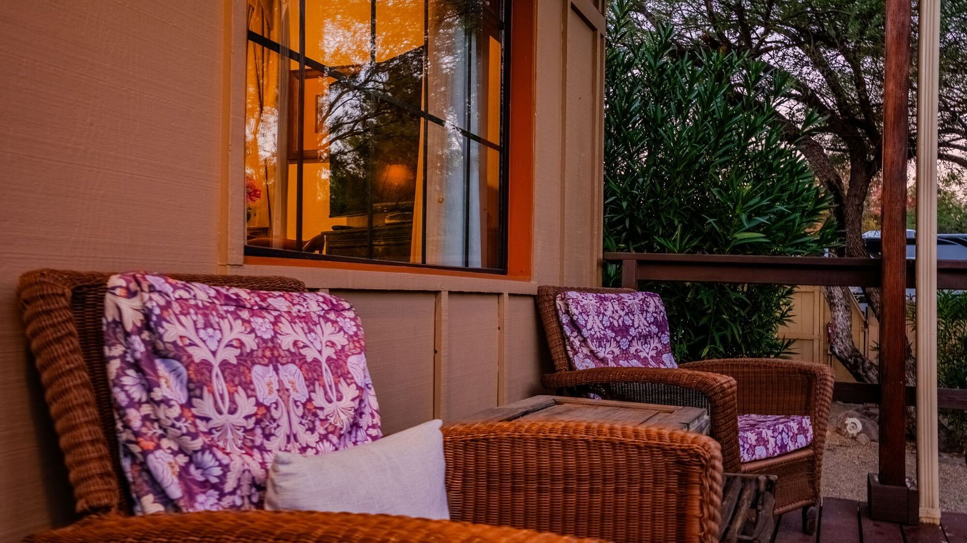 Two wicker chairs are sitting on a porch next to a window.