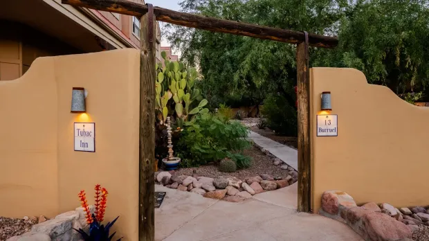 A wooden gate leading to a house with a cactus in front of it.
