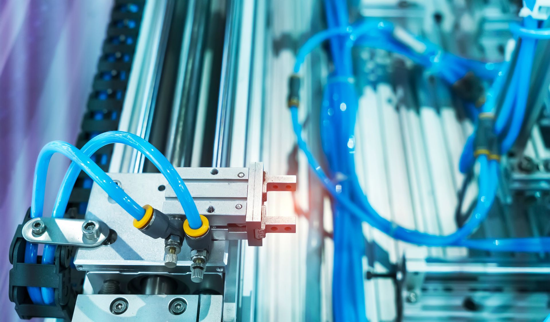 Primo piano di macchinari industriali con componenti in metallo argentato, tubi blu e connettori gialli.