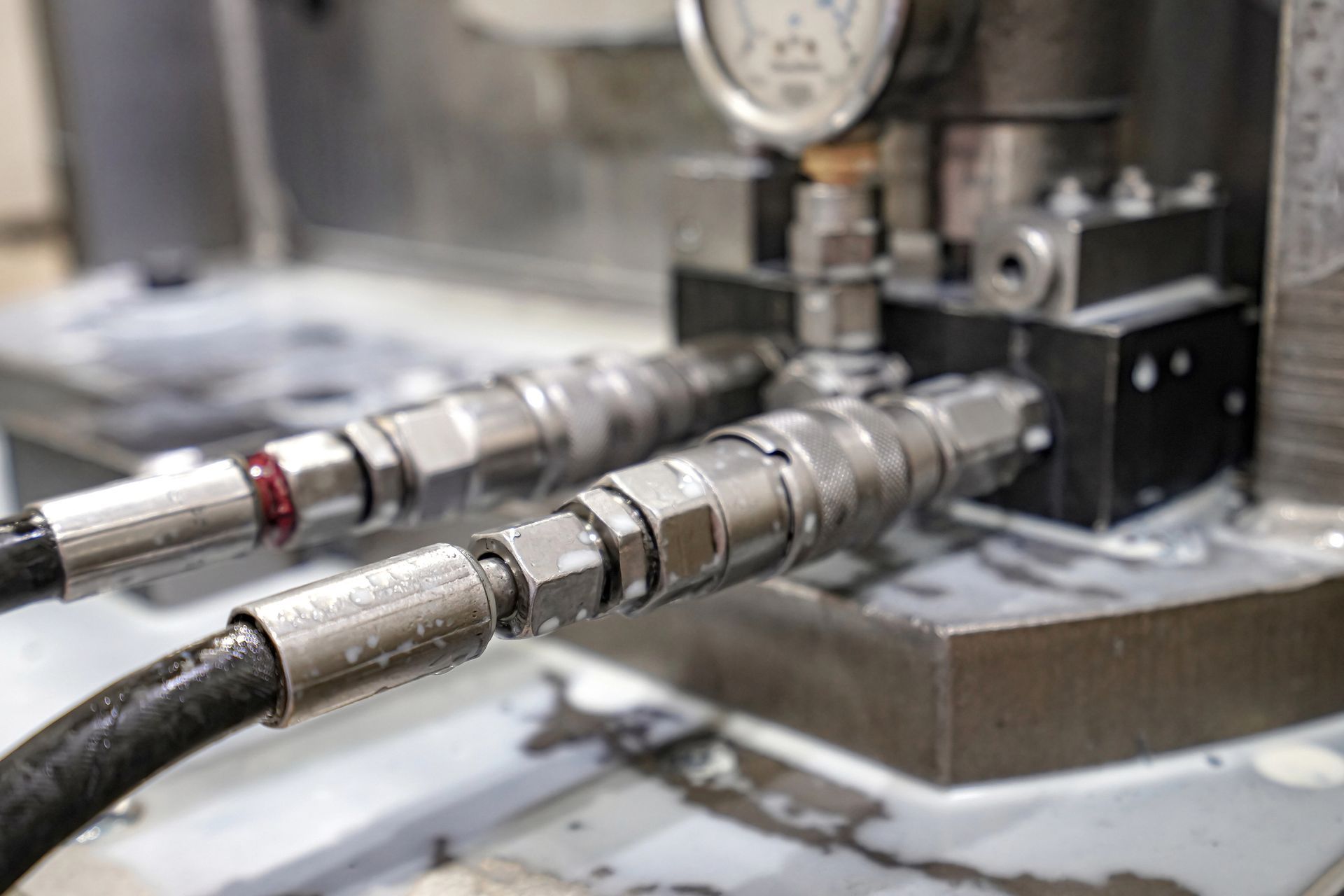 Primo piano dei tubi idraulici collegati a un blocco metallico con un manometro, presenza di refrigerante per la macchina.