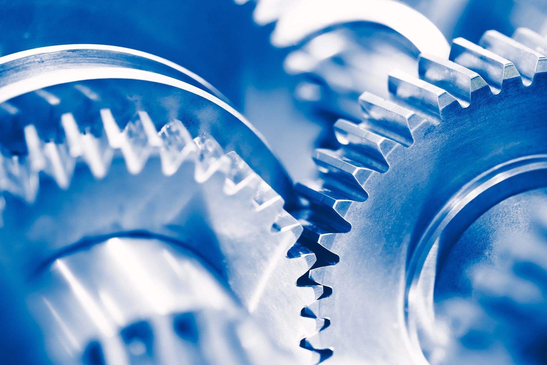 Primo piano di ingranaggi metallici interconnessi, in tonalità di blu, che suggeriscono la funzione meccanica.