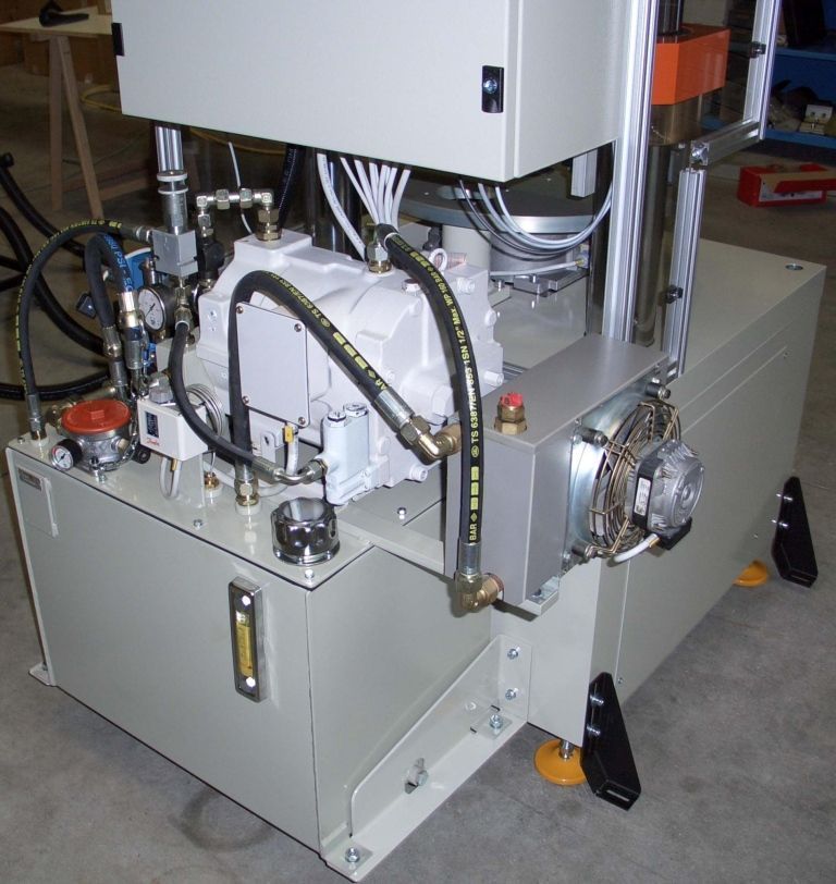 Sistema idraulico industriale grigio con tubi, serbatoio e componenti arancioni e neri.