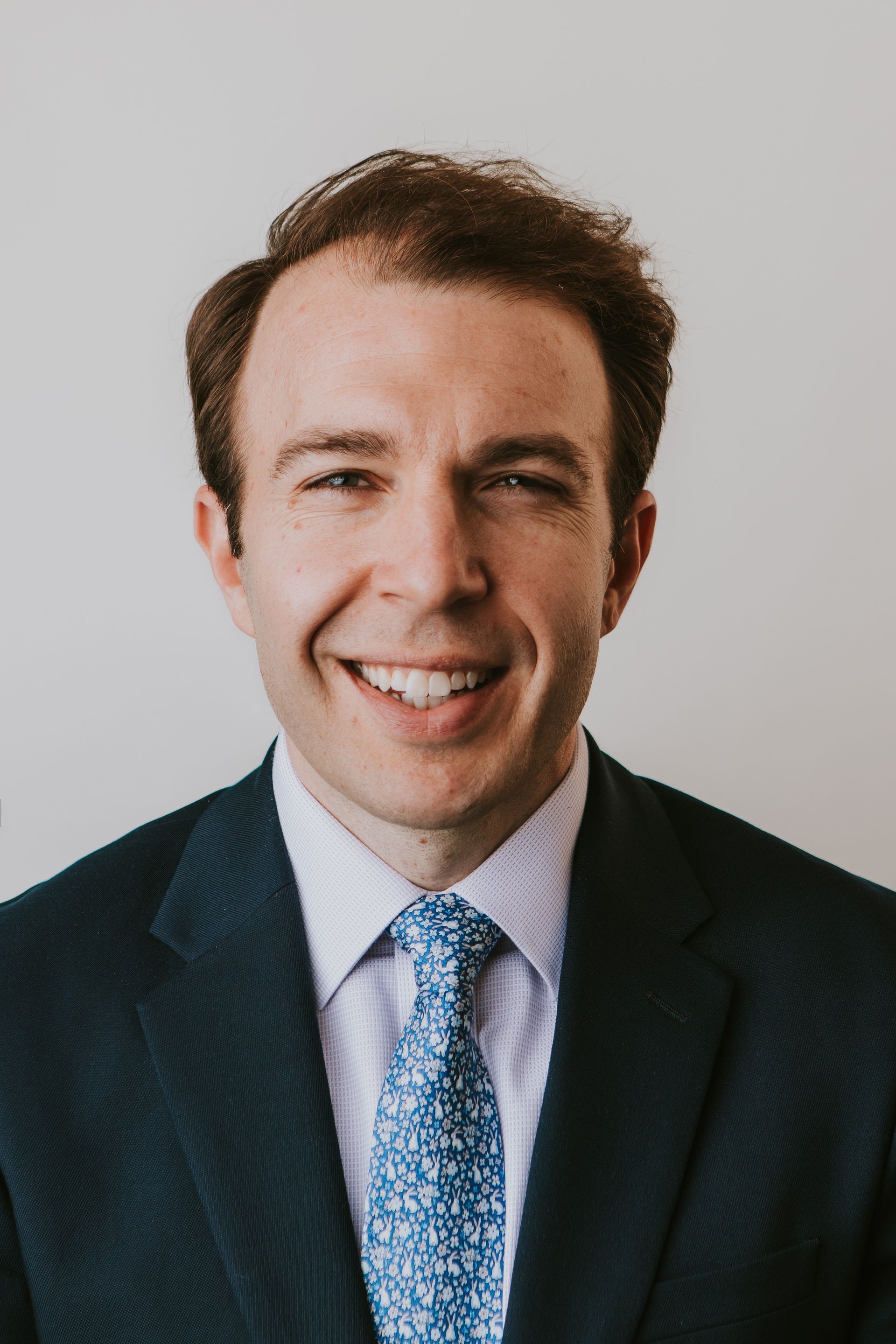 A man in a suit and tie is standing in front of a white wall.