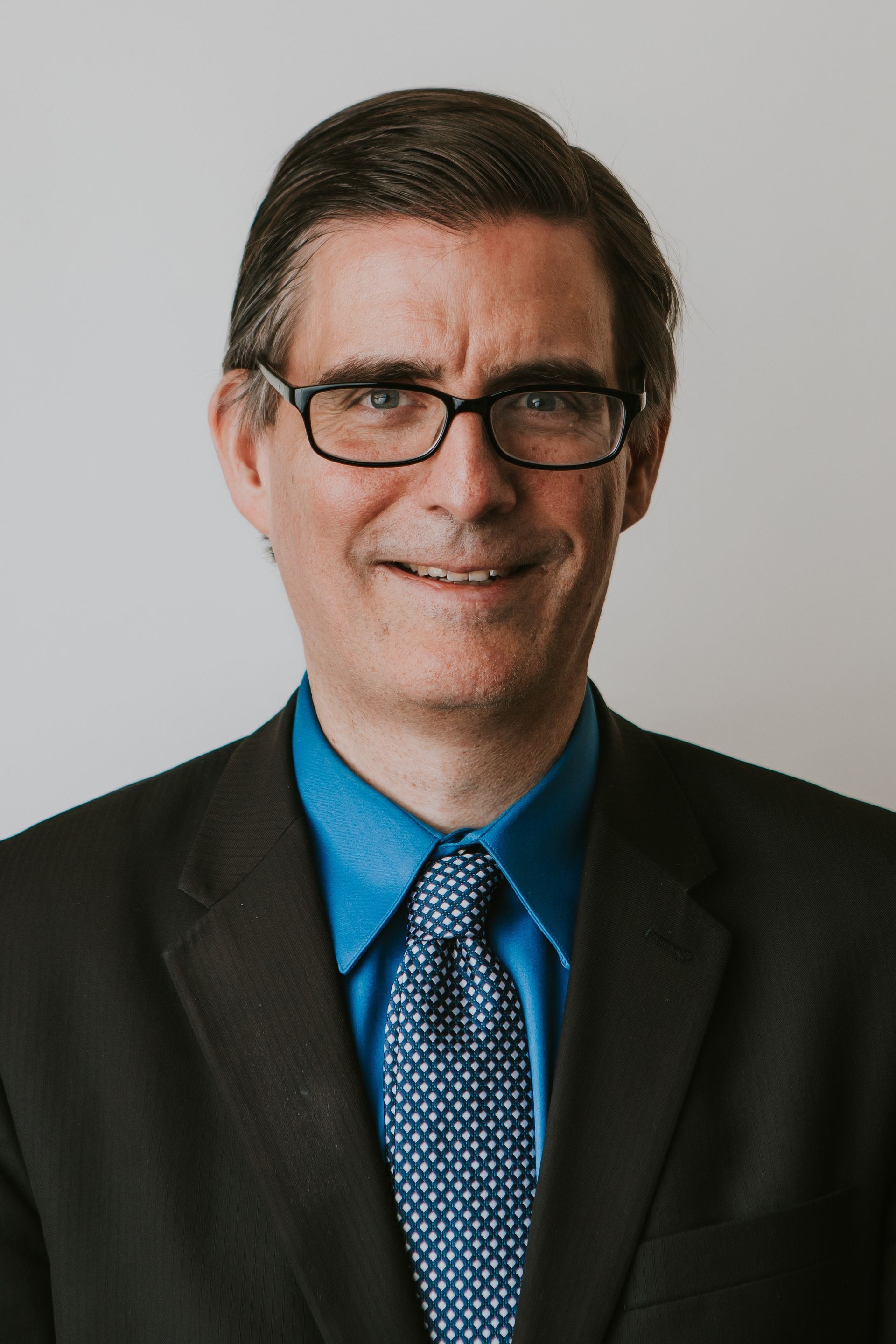 A man in a suit and tie is standing in front of a white wall.
