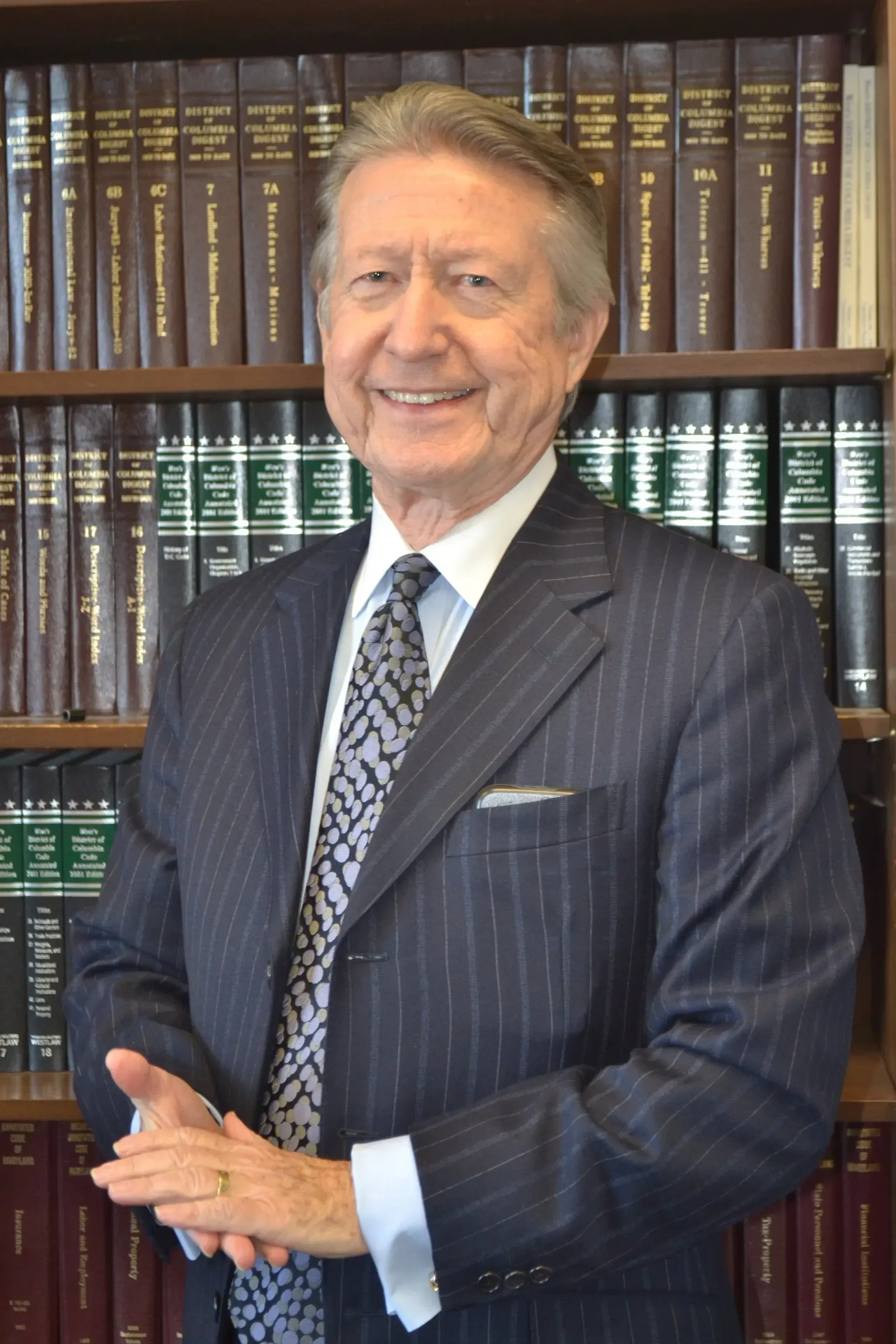 A man in a suit and tie is standing in front of a white wall.
