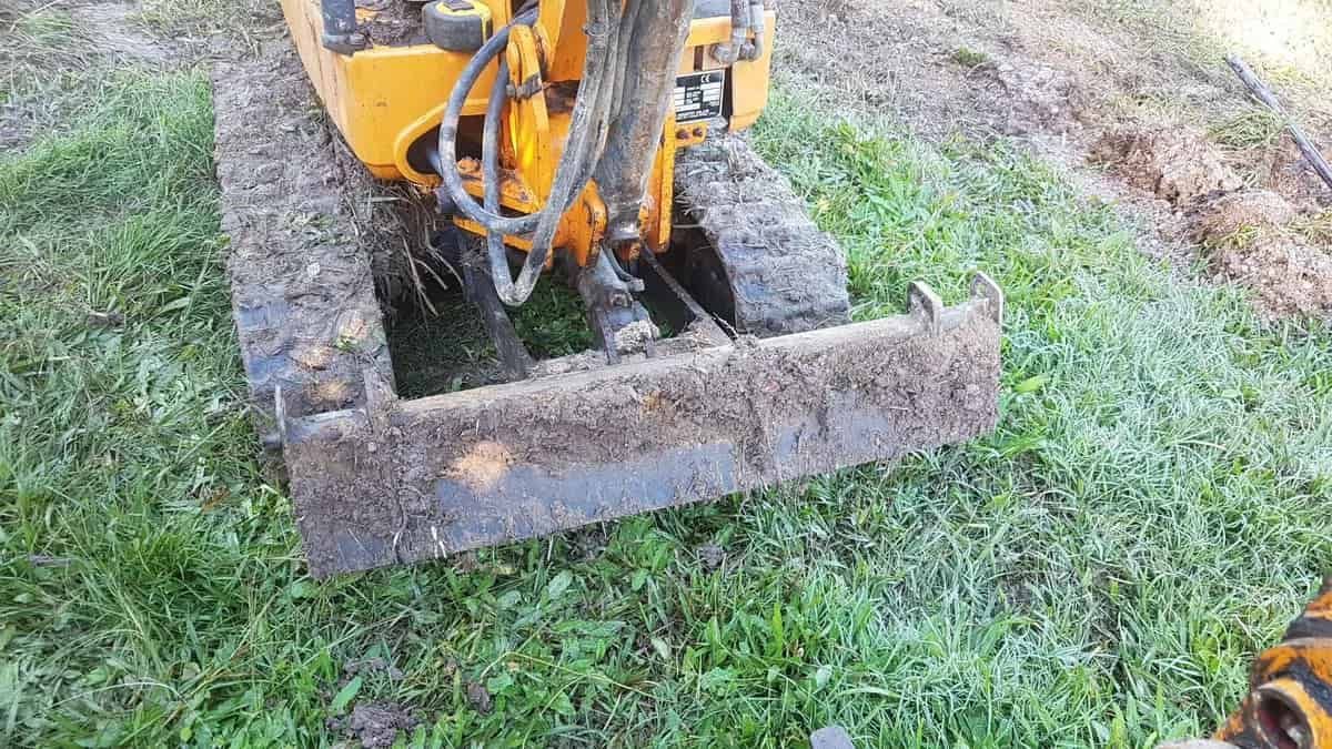 A Small Yellow Excavator Is Sitting On Top Of A Lush Green Field — Northern Rivers and Cape Hawke Septics in Forster, NSW