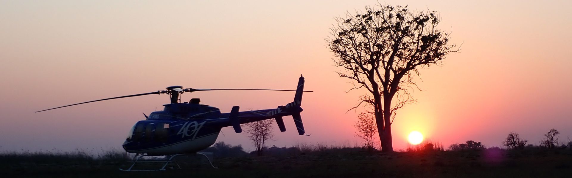 A helicopter is flying over a field at sunset.