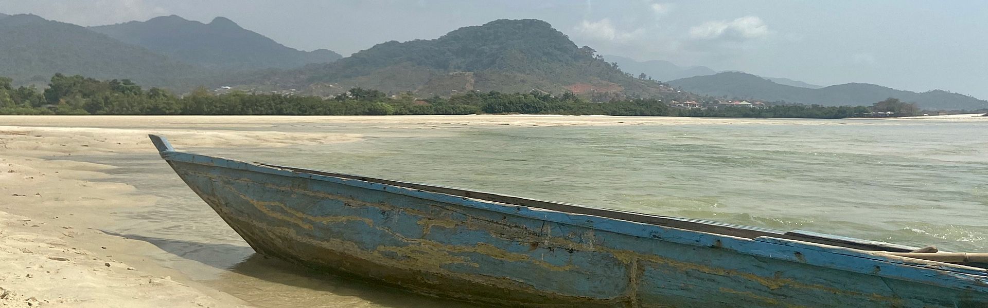 A blue boat is sitting on the beach near the water