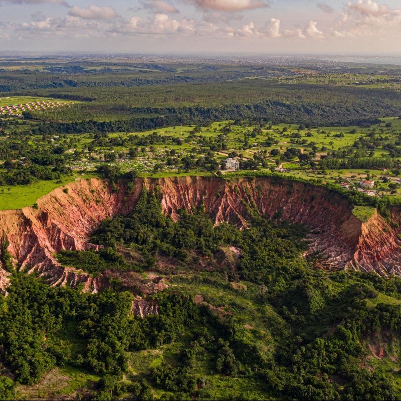An aerial view of a large crater in the middle of a lush green valley surrounded by trees.