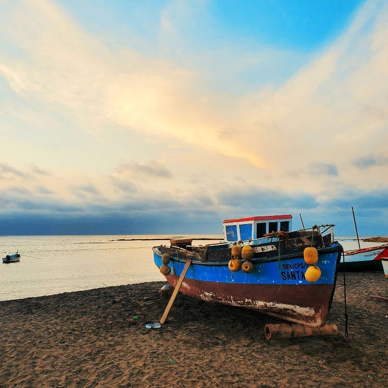 A fishing boat is sitting on the beach near the water.