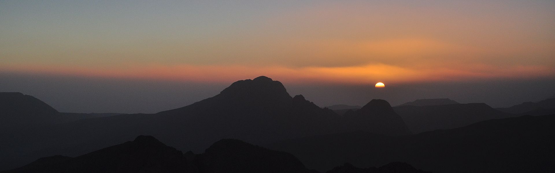 A helicopter is flying over a field at sunset.