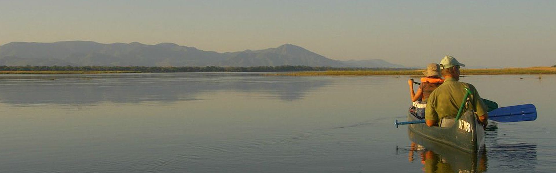 A person is paddling a canoe on a lake with mountains in the background.
