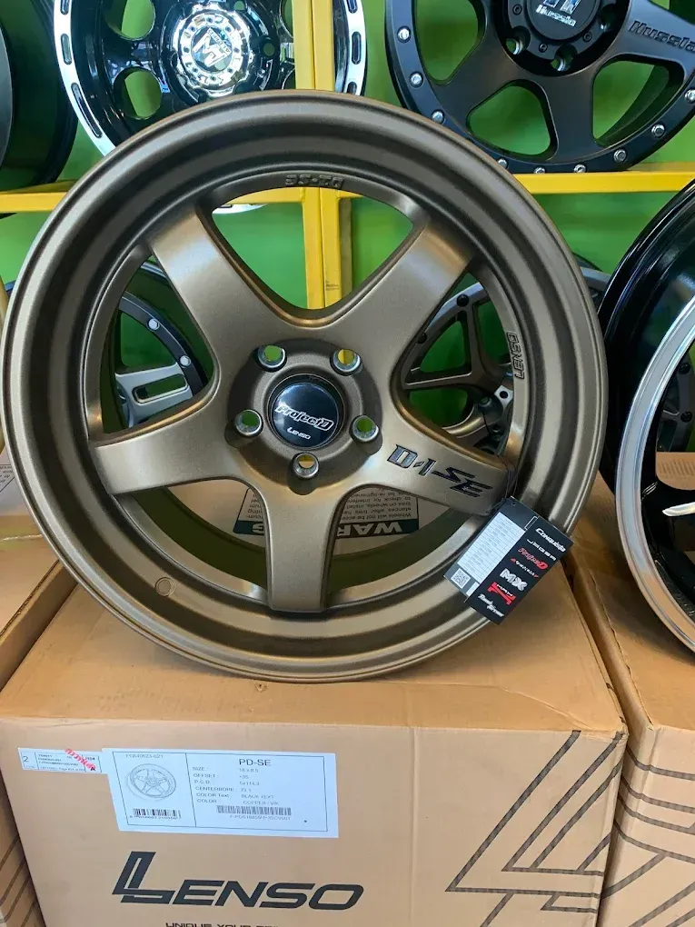 A bronze-colored Lenso D1-SE aftermarket car wheel resting on a cardboard box, displayed in a retail shop.