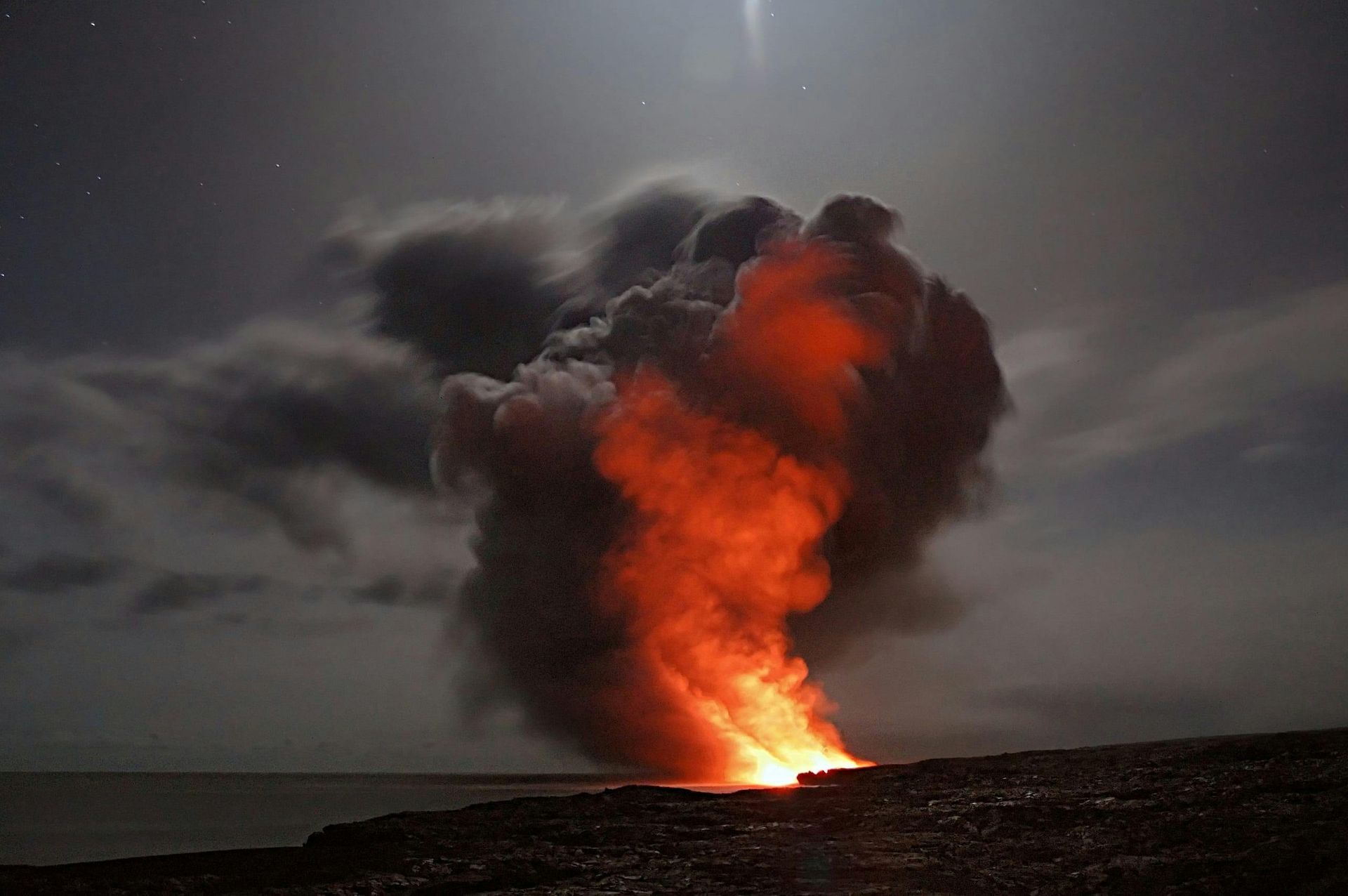 A volcano is erupting at night with a lot of smoke coming out of it.