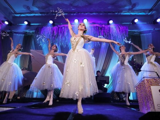 A group of women in white dresses are dancing ballet on a stage.