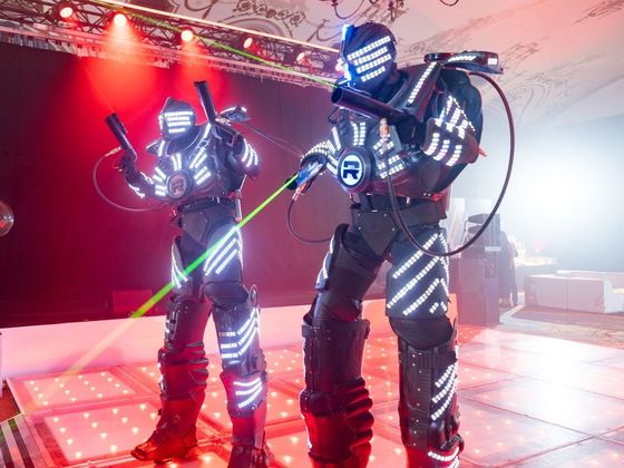 Two people in futuristic costumes are standing next to each other on a dance floor.