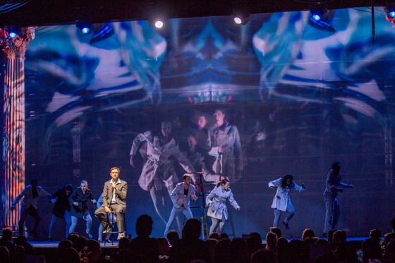 A group of people are dancing on a stage in front of a large screen.