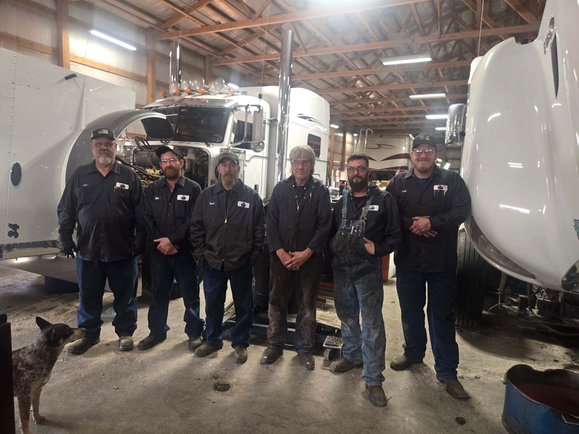 Semi-truck with open hood; engine exposed for repair. Grey truck parked outdoors, another truck in background.