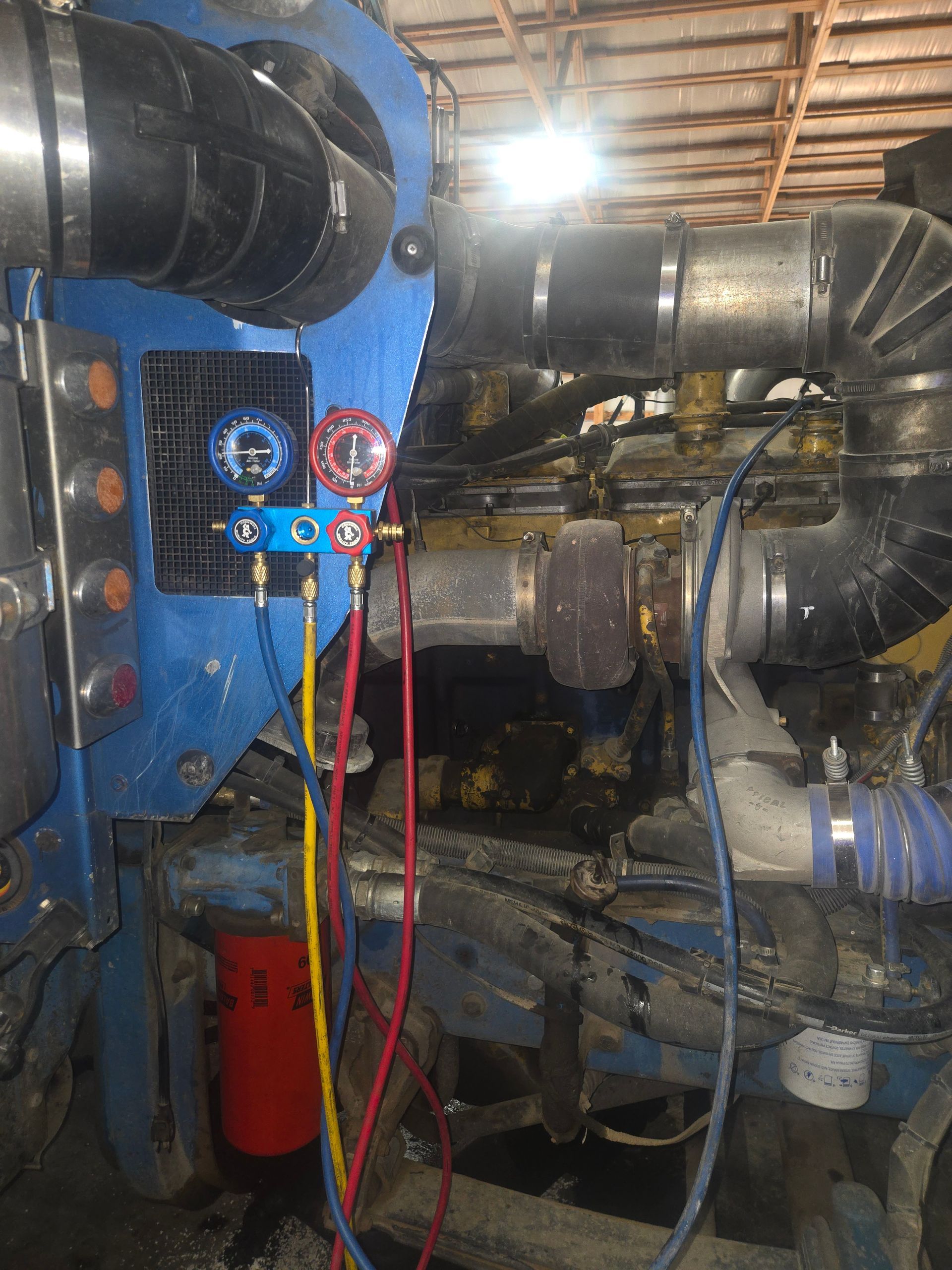 Mechanic in grey overalls working on a large truck with open hood, inside a garage.
