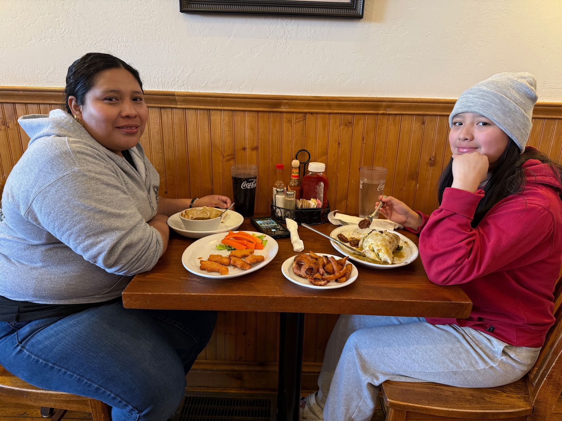 Two women are sitting at a table with plates of food on it.