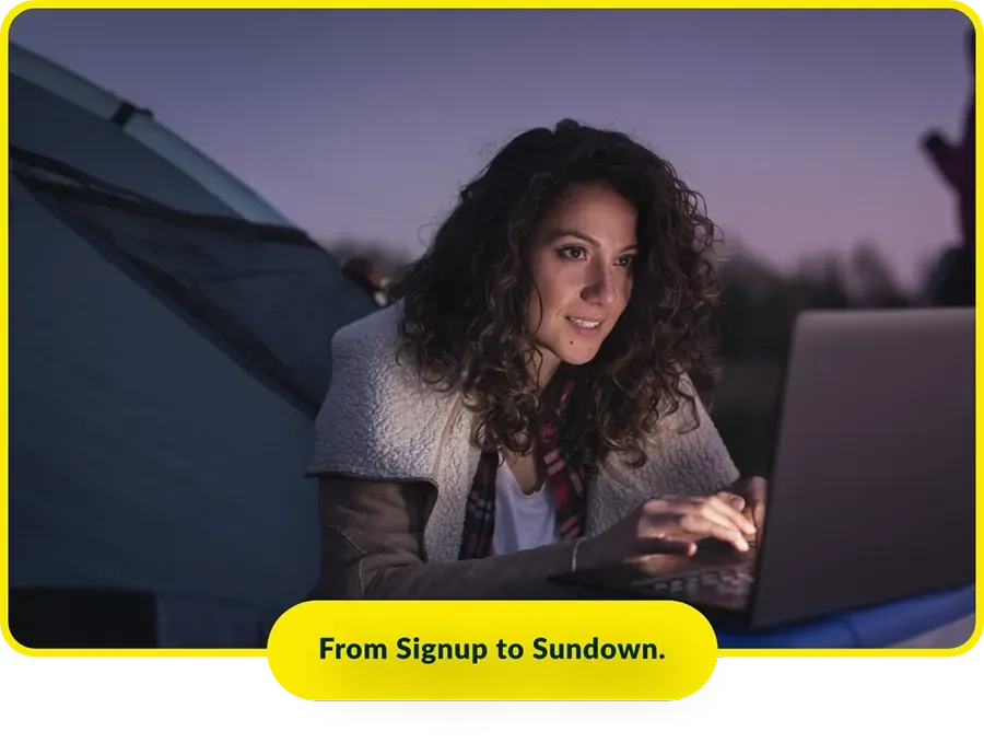 A woman is sitting in a tent using a laptop computer.