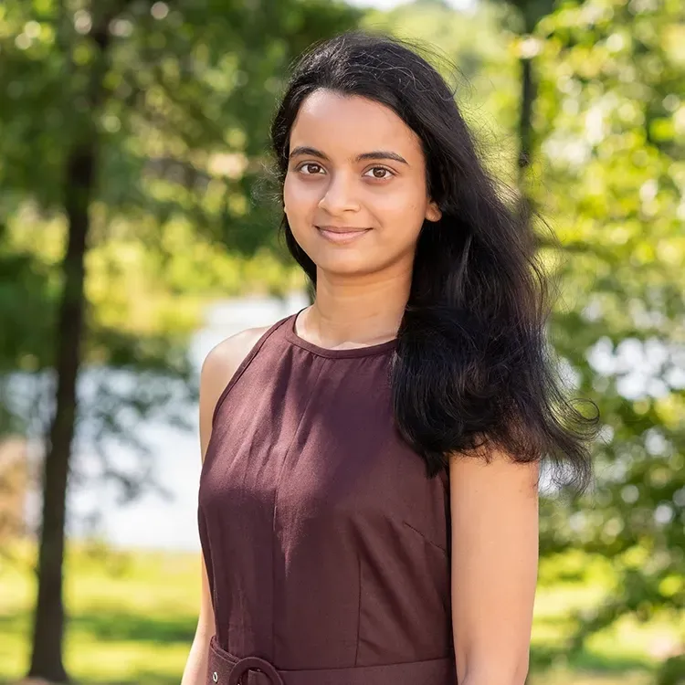 A young woman in a purple dress is standing in a park.
