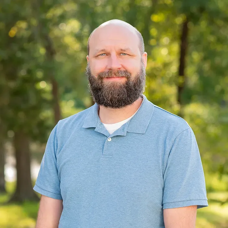 A bald man with a beard is wearing a blue polo shirt.