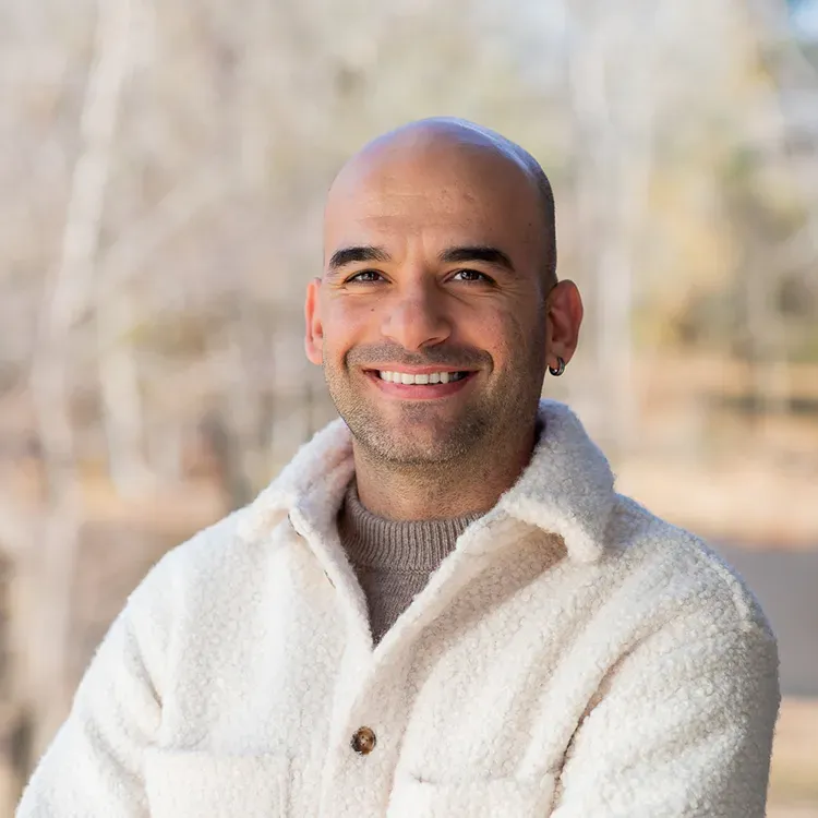 A bald man is wearing a white jacket and smiling for the camera.