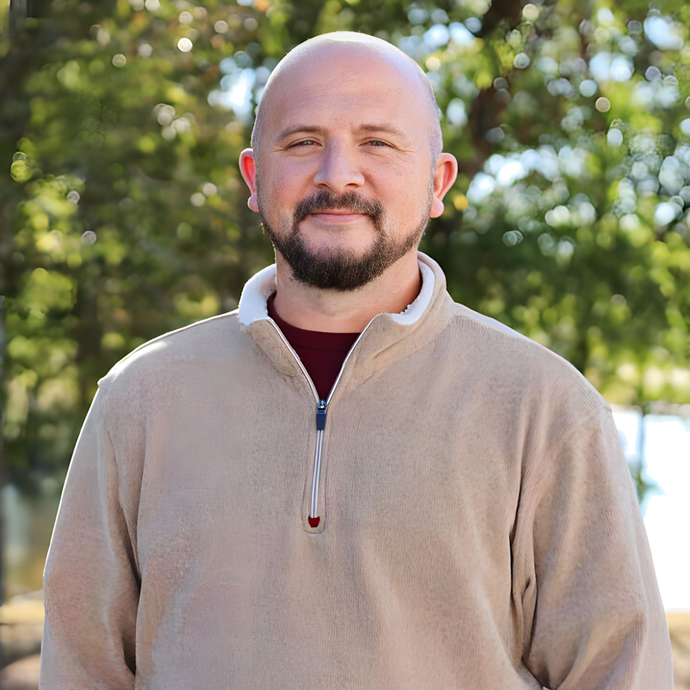 A bald man with a beard is wearing a tan sweater