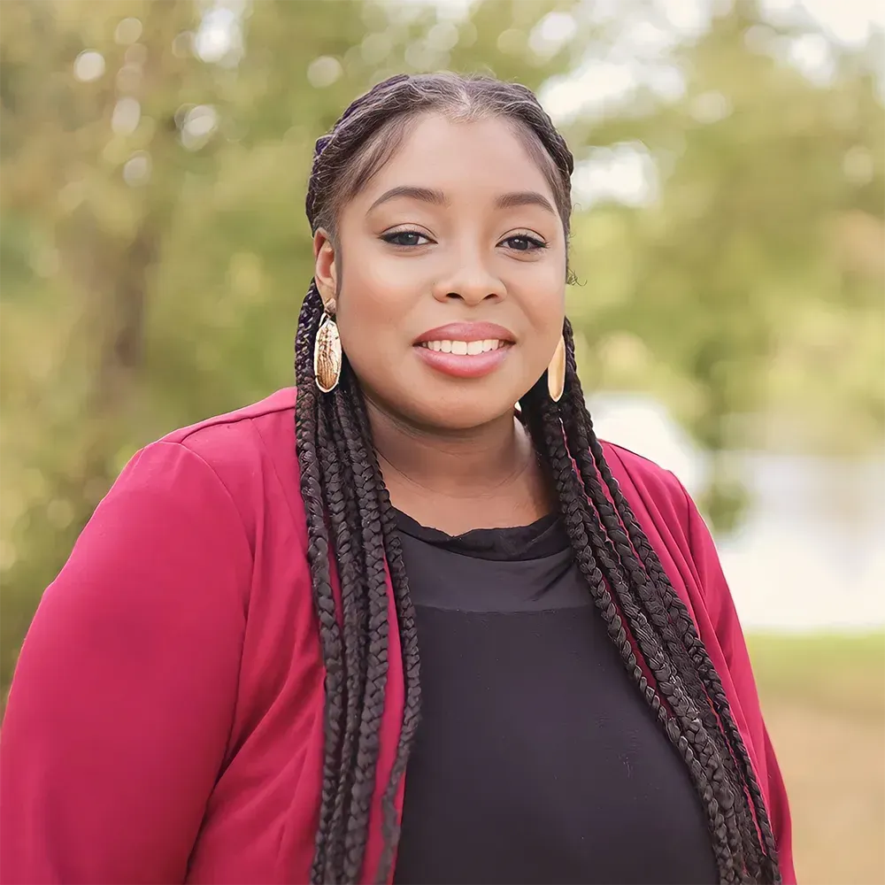 A woman with braids is wearing a red jacket and earrings.