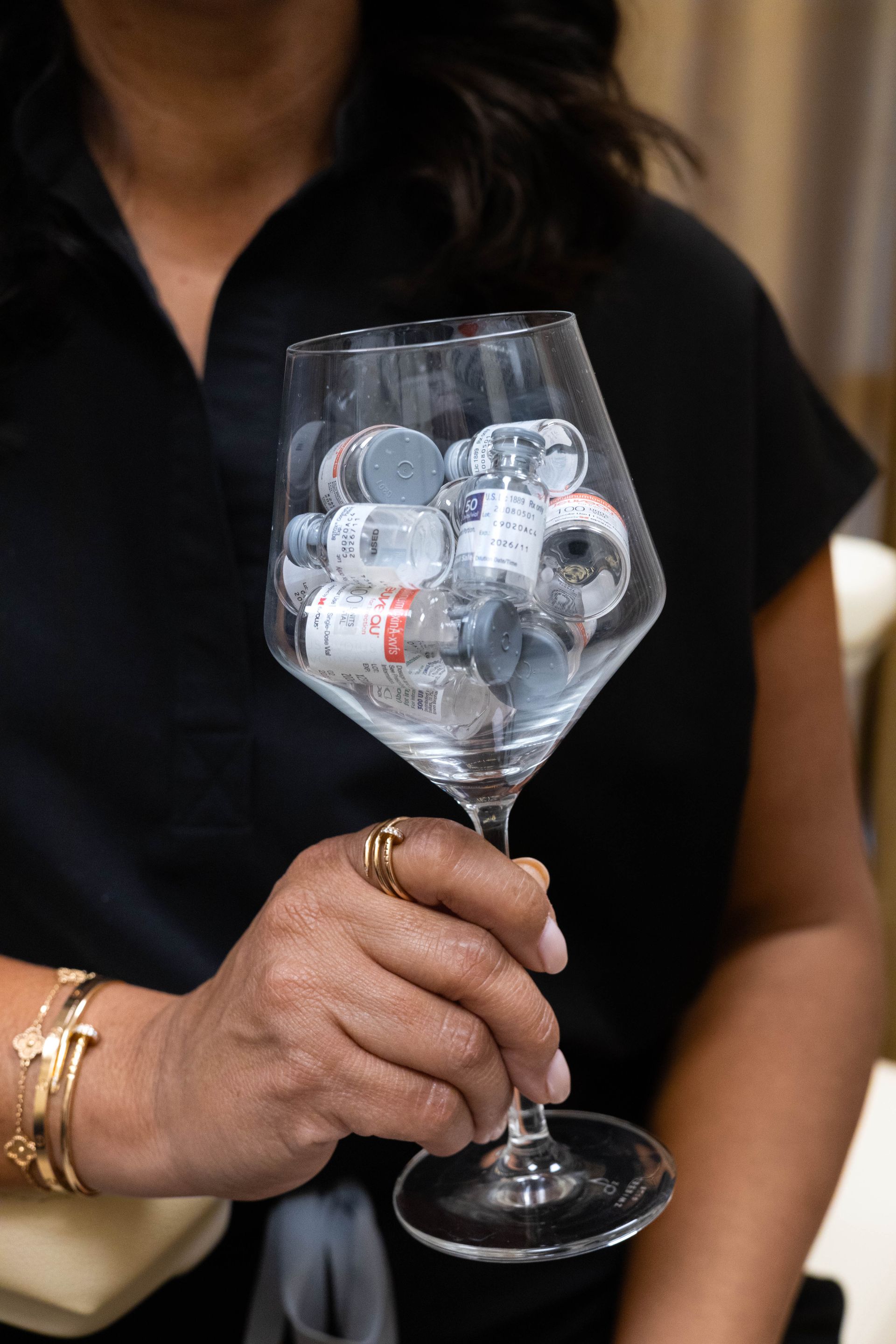 A person holds a wine glass filled with small medical vials.